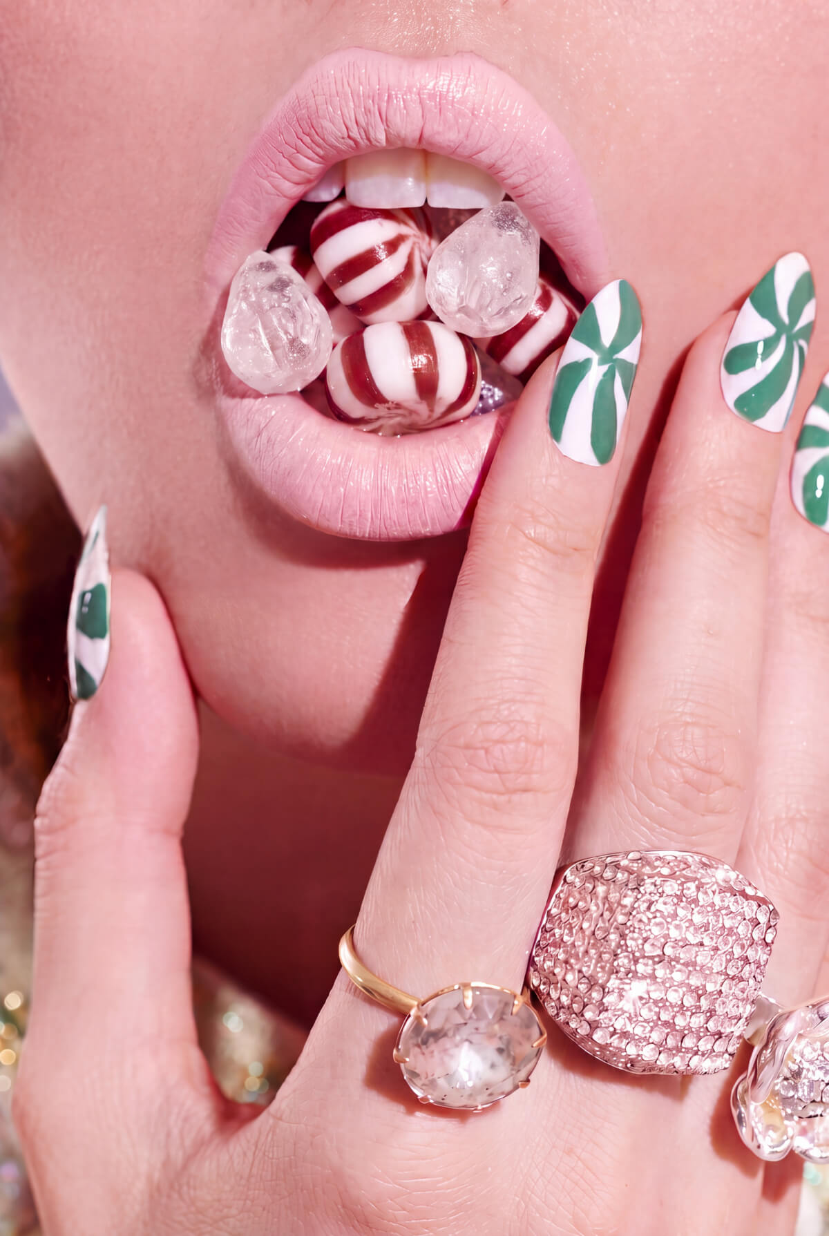 Green and white peppermint swirl nail art on almond nails, hand held to lips with striped boiled sweets and crystal rings